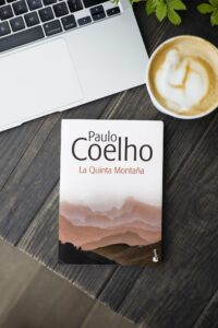 El libro La Quinta Montaña, de Paulo Coelho, al lado de una taza de café y un ordenador portátil