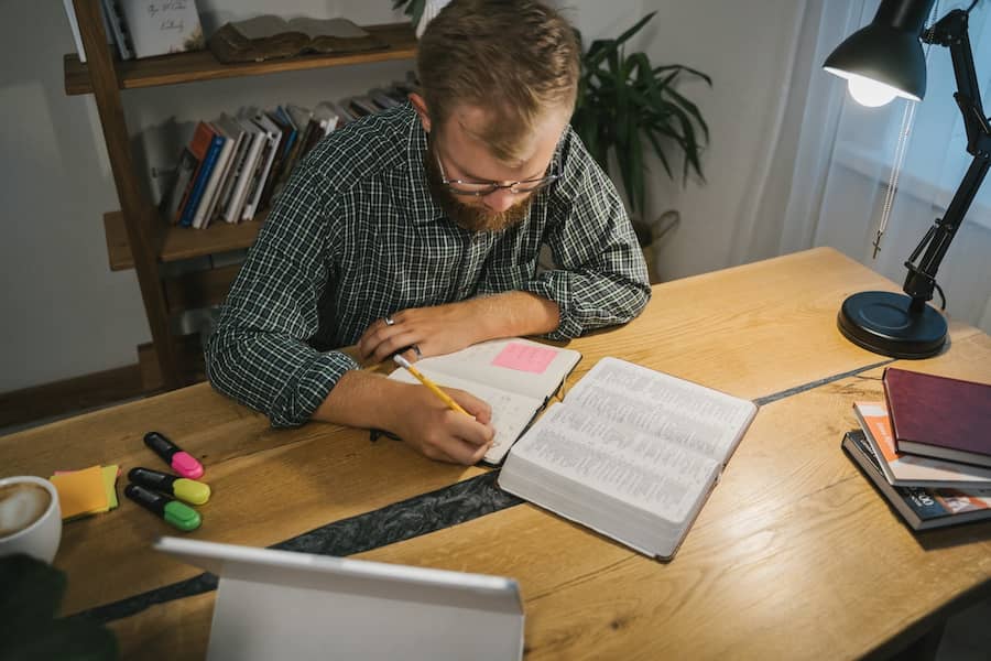 Un hombre en su mesa de estudio lee detenidamente y toma notas de la Biblia