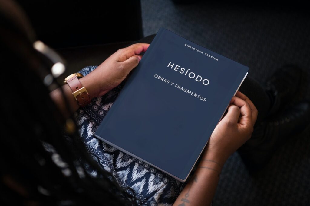 Una persona sentada sosteniendo un libro de Hesíodo titulado 'Obras y Fragmentos', que incluye 'Teogonía' y 'Los Trabajos y los Días', con una cubierta azul oscuro de la 'Biblioteca Clásica Gredos'.