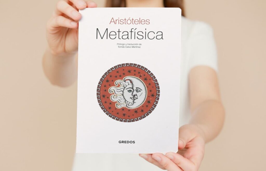 Manos sujetando el libro 'Metafísica' de Aristóteles con cubierta de la editorial Gredos.